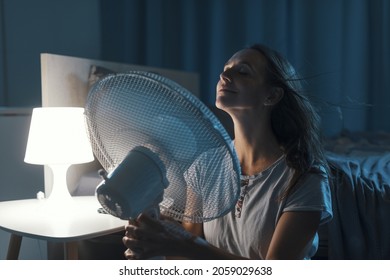 Woman In Her Bedroom On A Hot Summer Night, She Is Enjoying Fresh Air In Front Of A Fan