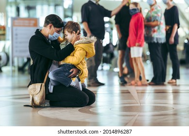 Woman And Her Boy Sitting On Floor At Airport. Mother In Face Mask Sitting With Her Son At International Airport Terminal.