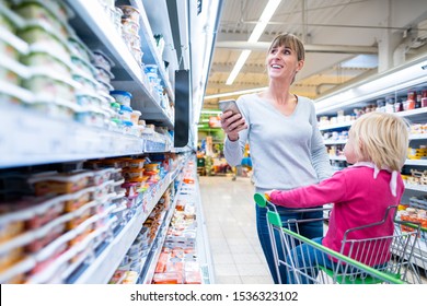 Woman With Her Child In Fresh Department Of Supermarket Having The Shopping List On Her Phone