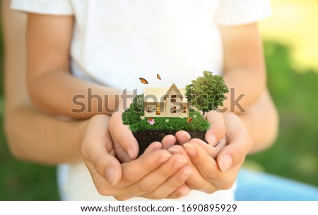 Woman and her child holding their dream house with beautiful green lawn on sunny day, closeup