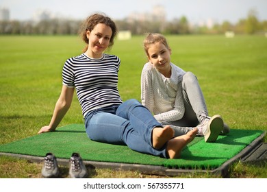 Woman and her daughter sits on green golf course after game at sunny day