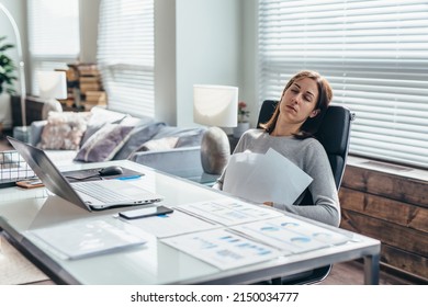 Woman at her desk asleep sitting on a chair holding paper to her chest