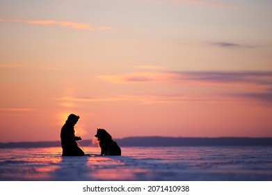 Woman with her dog on a frozen lake ice. Cold winter day, sun setting in the horizon, Eastern Finland.