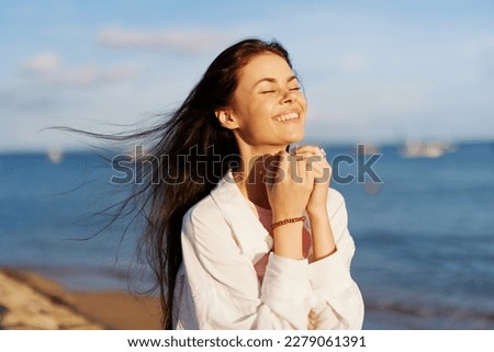 A woman with her eyes closed in the sun on a horse on the ocean smile, flying hair, tanned skin, rest, the concept of skin care in summer and spring.