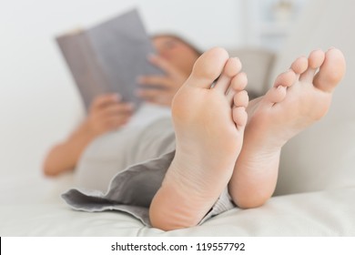 Woman With Her Feet Up Reading A Book On The Sofa