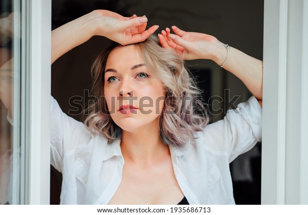 Woman in her flat getting dressed\
near window frame. French style. Modern colorful\
hairstyle.