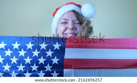 A woman in her forties holding a US flag in the background. Portrait of a woman in a red Christmas hat. Holiday is joy