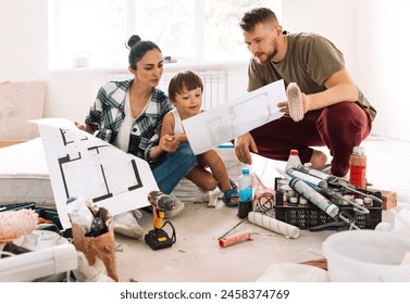 Woman with her husband and child are sitting on mattress among building materials and inventory. Married couple with cute kid are looking at house plan and discussing repairs. Apartment renovation. - Powered by Shutterstock