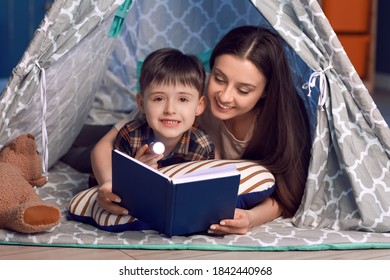 Woman And Her Little Son Reading Book In Play Tent At Night