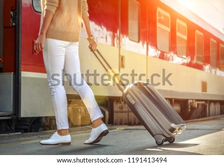 Woman with her luggage go  to red train on the peron of rail station under sun light at sunny day.