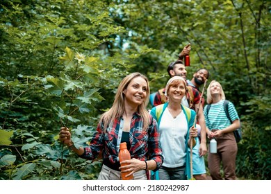 Woman with her multiethnic friends walking in woods. Smiling Female enjoying in hiking with hikers on wild trail among green trees. Copy space
