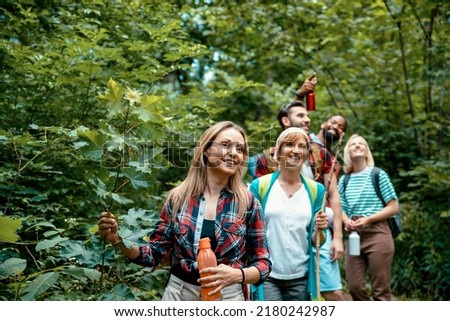 Woman with her multiethnic friends walking in woods. Smiling Female enjoying in hiking with hikers on wild trail among green trees. Copy space