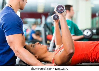 Woman With Her Personal Fitness Trainer In The Gym Exercising With Dumbbells