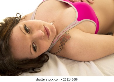 a woman in her pink bra laying in her bed with a serious expression.