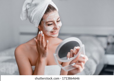 Woman in her room making facial mask holding mirror in his hands. Morning skin care routine. Stay at home while quarantined to avoid coronavirus.