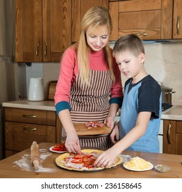 Woman And Her Son Making Pizza At Home. Teenager Boy Cooking With His Mother.