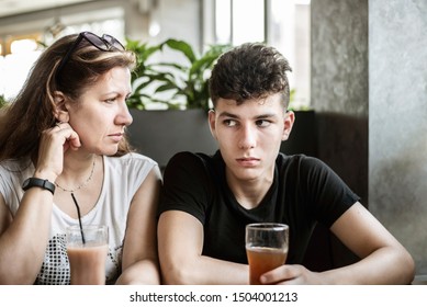 Woman With Her Teenage Son Sit In A Cafe And Drink Juice, They Have Sad, Serious Faces, They Try To Reconcile After Quarrel. The Boy Has A Difficult Character And His Mother Tries To Understand Him