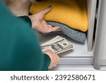 woman hides American dollars in a closet with clothes. stash of dollars