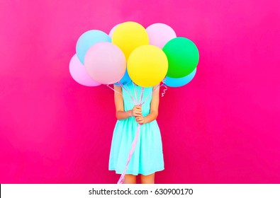 Woman is hides her head an air colorful balloons having fun over pink background