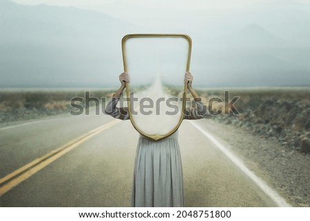 the woman hides holding a mirror in front of her face; introspection path concept Imagine de stoc © 