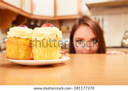 Woman hiding behind table sneaking and looking at delicious cake with sweet cream and fruits on top. Appetite and gluttony concept.