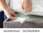 Woman hiding dollar banknotes under mattress in bedroom, closeup. Money savings