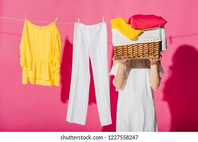 Woman Hiding Face Behind Wicker Basket With Hanging Clothes At Background