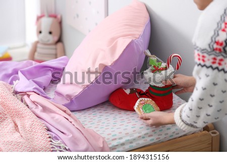 Woman hiding present under pillow in children's bedroom, closeup. St. Nicholas day