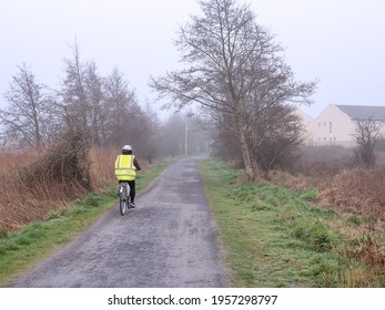 Woman in high visibility vest and helmet riding bicycle on a small road into fog. Safety on the road concept. Outdoor sport and healthy life style