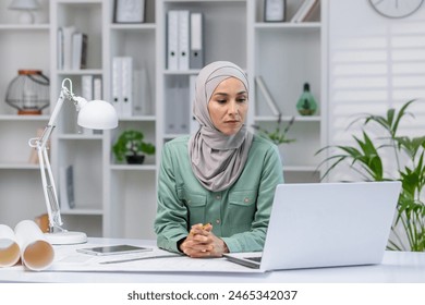 Woman in hijab designer working in home office, architect using laptop at work, studying technical assignment online, serious and concentrated reading. - Powered by Shutterstock