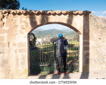 Woman hiker or backpacker looking into private almond orchard through ols stony entrance gate. 