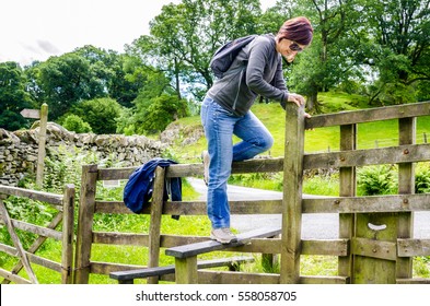 Woman Hiker Climbing A Fence Along A Path Through The Countryside