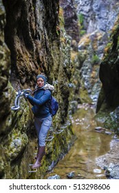 Woman Hiker Climbing On Safety Chains Through A Very Narrow Gorges