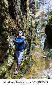 Woman Hiker Climbing On Safety Chains Through A Very Narrow Gorges