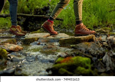 Woman Hiker Crossing A Small Forest Stream In A Close Up Low Angle View Of Her Feet In Leather Boots On Natural Rock Stepping Stones