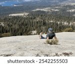 Woman hiker resting on granite outcropping vista of Central Sierras and Shaver Lake