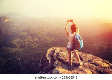 woman hiker taking photo with smart phone at mountain peak cliff