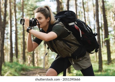Woman hiker taking photos using modern mirrorless camera in green forest