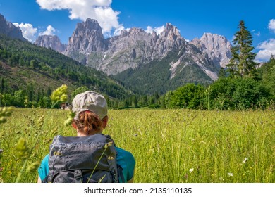 Woman Hiker Trekking In A Meadow At The Base Of Pale Di San Martino Mountain Range - Blurred Background. San Martino Di Castrozza, Trentino, Italy