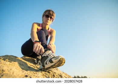 Woman hiker tying shoe laces of her sport boots while climbing steep big rock on a sunny day. Young female climber overcomes difficult climbing route. Active recreation in nature concept.