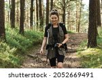 Woman hiker walking with a backpack and modern mirrorless camera in green forest