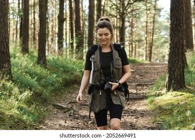 Woman hiker walking with a backpack and modern mirrorless camera in green forest