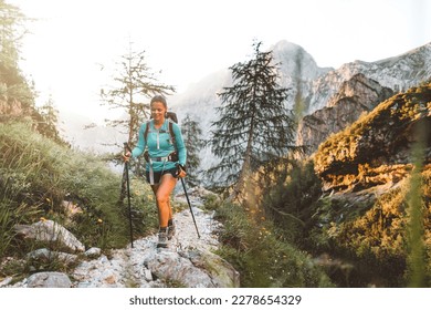 Woman hiker walking with hiking poles on a rocky mountain trail early in the morning on a beautiful summer day - Powered by Shutterstock