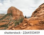 Woman hiker walking on Bell Rock trail in red rock formations within coconino national forest in Sedona Arizona USA against white cloud background.
