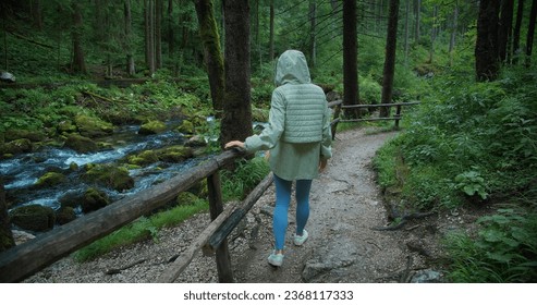 Woman hiker walks along mountain river in coniferous forest at rainy day. Outdoor activity and travel in nature. - Powered by Shutterstock