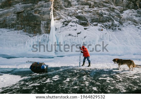 Woman hiker in winter hike drilling ice on  frozen lake with a drill