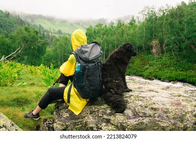 Woman Hiker In Yellow Raincoat Rest With Black Dog Near By The Mountain River In The Rain