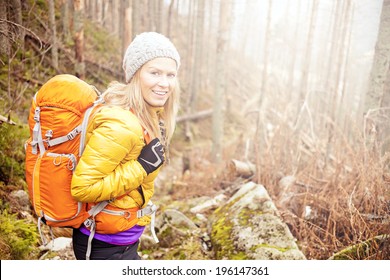 Woman Hiking In Autumn Forest In Mountains. Trekking, Recreation And Healthy Lifestyle Outdoors In Nature. Beauty Blond Backpacker Looking At Camera Smiling, Bright Light Sunlight In Background.