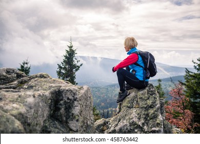 Woman Hiking In Autumn Mountains And Woods. Sitting On Rock And Relaxing, Recreation And Healthy Lifestyle Outdoors In Fall Nature. Beauty Blond Looking At Sunset Inspirational Landscape View.