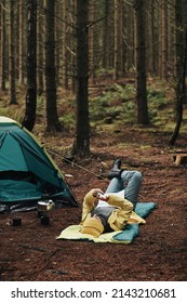 Woman In Hiking Gear Checking Her Cellphone While Lying On Her Sleeping Bag At Her Campsite In The Morning